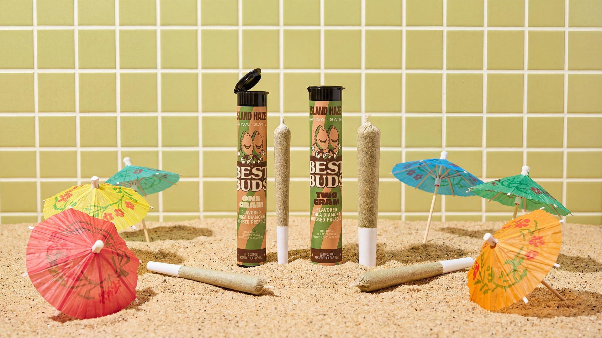 Cannabis products with decorative umbrellas on a sandy surface against a tiled wall.
